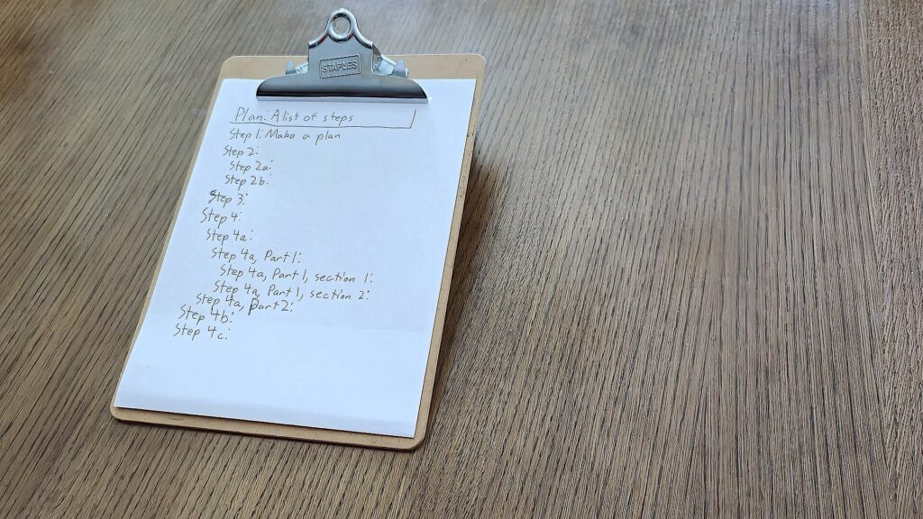Klemmbrett mit einer teilweise abgehakten Liste, daneben liegt ein Kugelschreiber auf dem Tisch