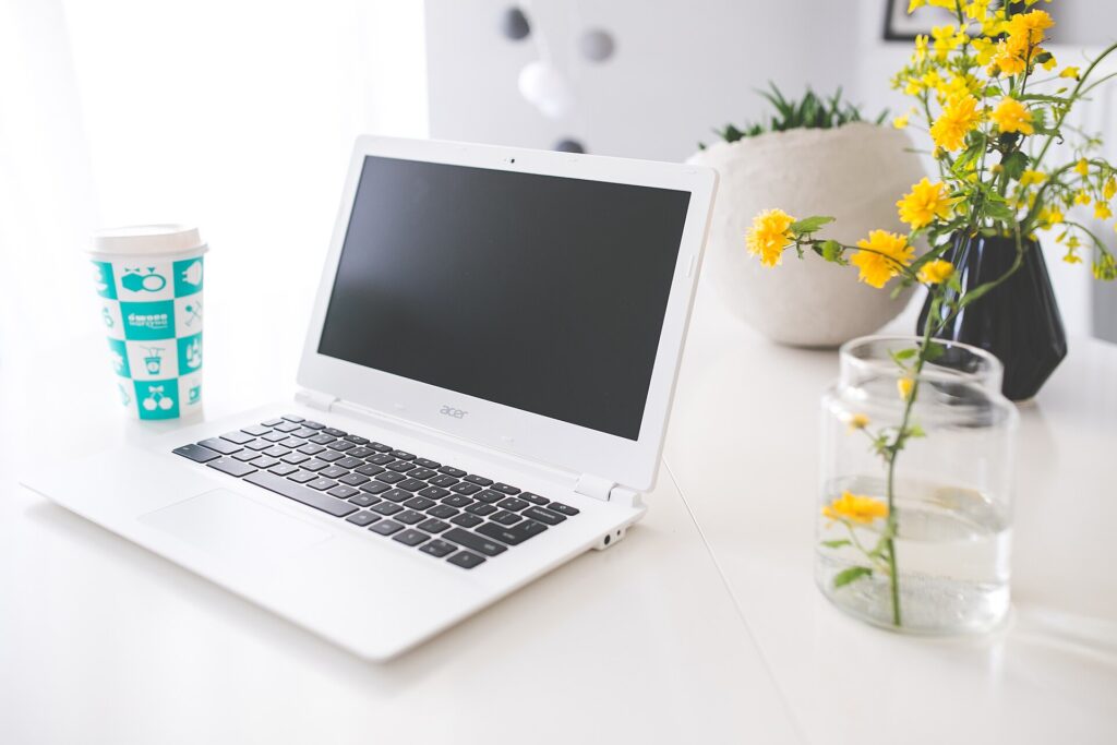 Laptop und aufgeschlagenes Notizbuch auf einem Schreibtisch, daneben Stift und Kaffeetasse