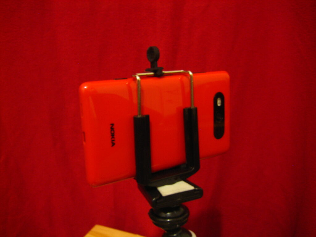 Smartphone auf einem kleinen Stativ vor einem Tisch mit Produkten und einer Lampe