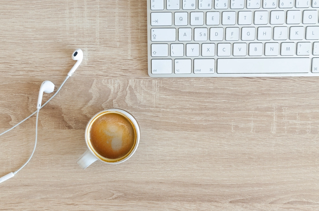 Tastatur auf einem Schreibtisch, daneben eine Tasse Kaffee und ein Stift