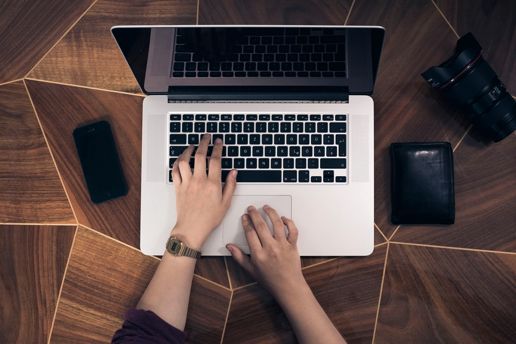Laptop und Smartphone nebeneinander auf einem Schreibtisch, daneben ein Notizblock mit Zahlen