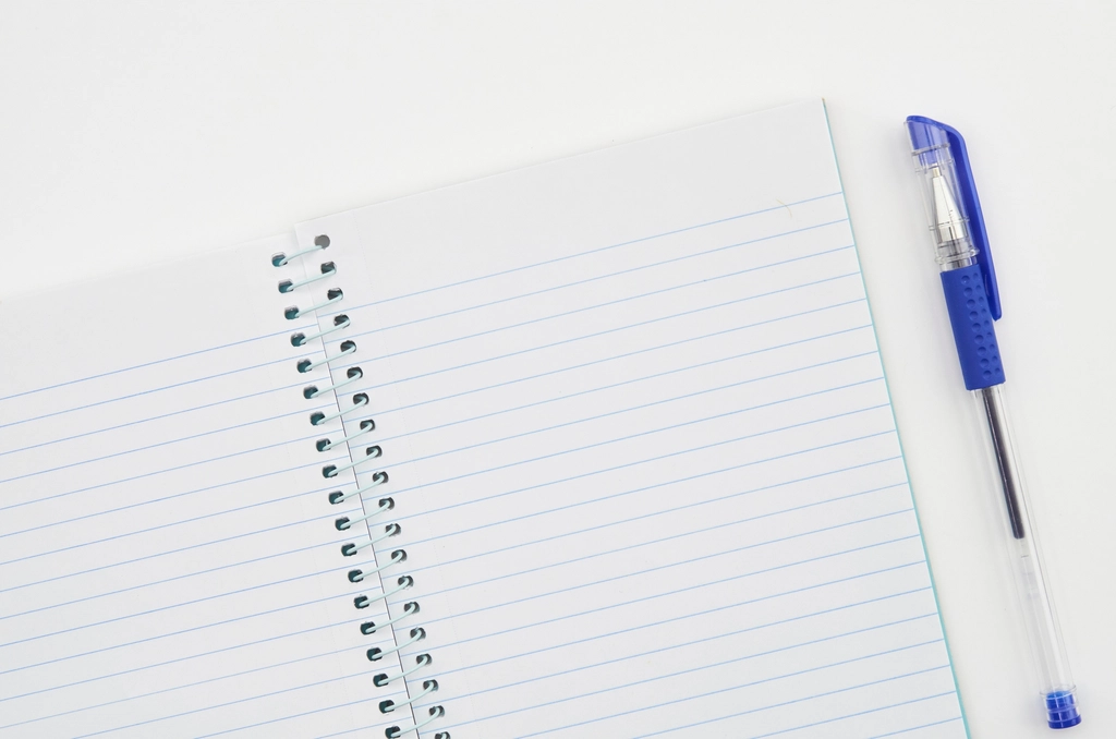 Aufgeschlagenes Notizbuch mit handschriftlicher Tabelle, daneben liegt ein Kugelschreiber auf dem Tisch